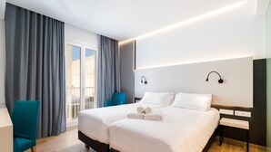 Quarto de hotel moderno com cama de casal, escrivaninha, cadeira e uma grande janela com cortinas.