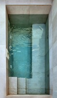 Uma banheira retangular com superfície de água límpida, rodeada por paredes revestidas de azulejos.