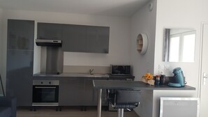 Una cocina moderna con armarios grises, horno empotrado, microondas y una pequeña zona de comedor con una silla negra.
