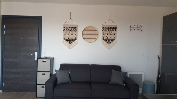 Una sala moderna con un sofá oscuro, dos tapices de macramé, un espejo redondo y un calentador empotrado.