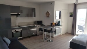 Una cocina moderna con electrodomésticos de acero inoxidable, un área de comedor con un taburete de bar y un sofá.