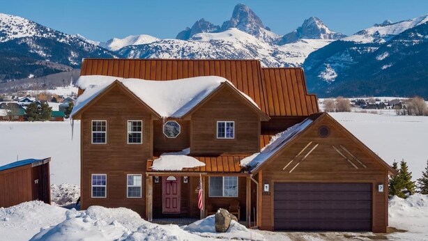Una casa de madera de dos pisos con garaje, rodeada de nieve y montañas.