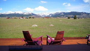 Una terraza con dos sillas Adirondack con vista a un campo cubierto de hierba y montañas al fondo.