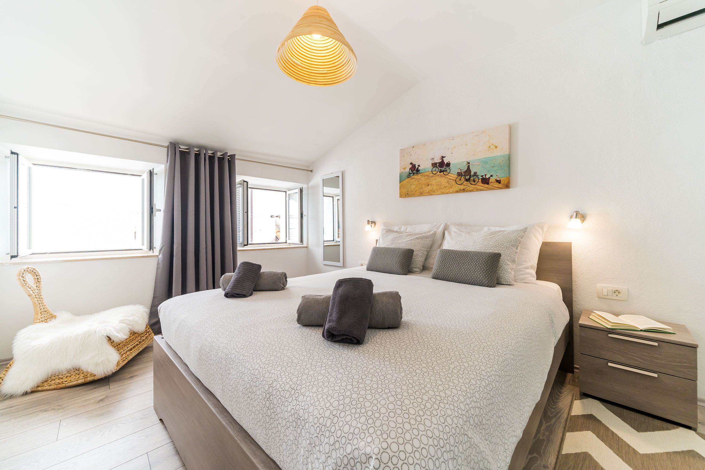 A bedroom with a large bed, a bedside table with a lamp, a wall-mounted painting, and a window with curtains.