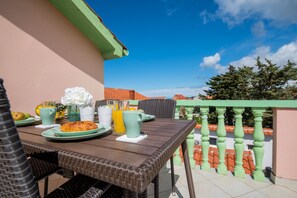 A dining table set with plates, cups, and a pastry, surrounded by wicker chairs on a balcony with a green railing and a clear blue sky. - Modern 2BR Beach Apartment in Zadar (Zadar)