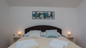 A neatly made bed with white linens and two rolled towels, a dark headboard, and a wall-mounted abstract art piece. - Modern 2BR Beach Apartment in Zadar (Zadar)