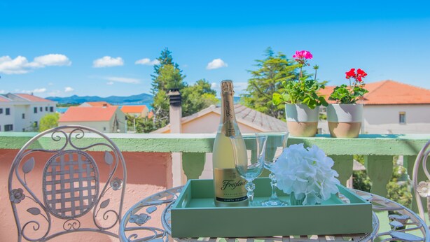 A balcony with a bottle of Freixenet champagne, two glasses, and a flower arrangement on a tray. - Modern 2BR Beach Apartment in Zadar (Zadar)