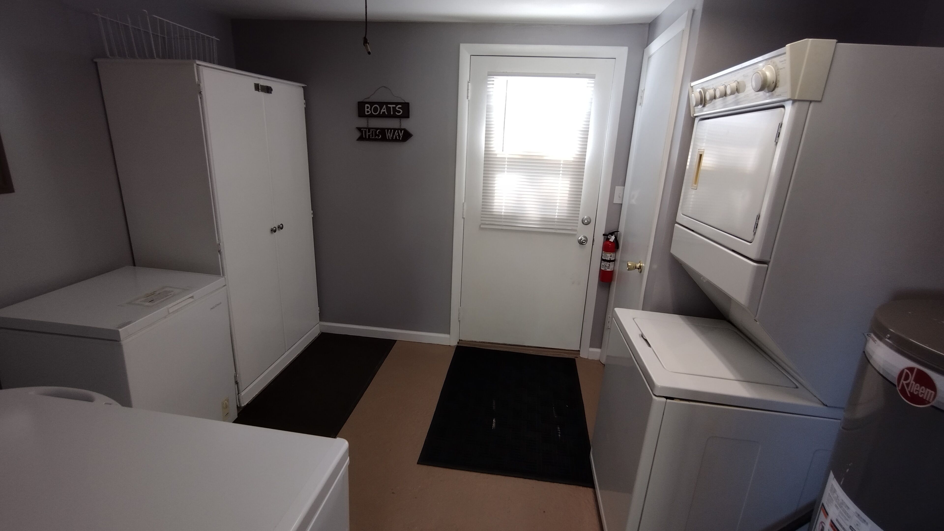 A compact kitchen with white appliances, a black and beige floor mat, and a door with a sign reading "BOATS THIS WAY".