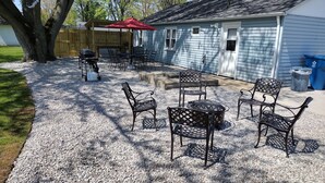 Un patio al aire libre con una parrilla, asientos y una mesa cubierta con un paraguas rojo.