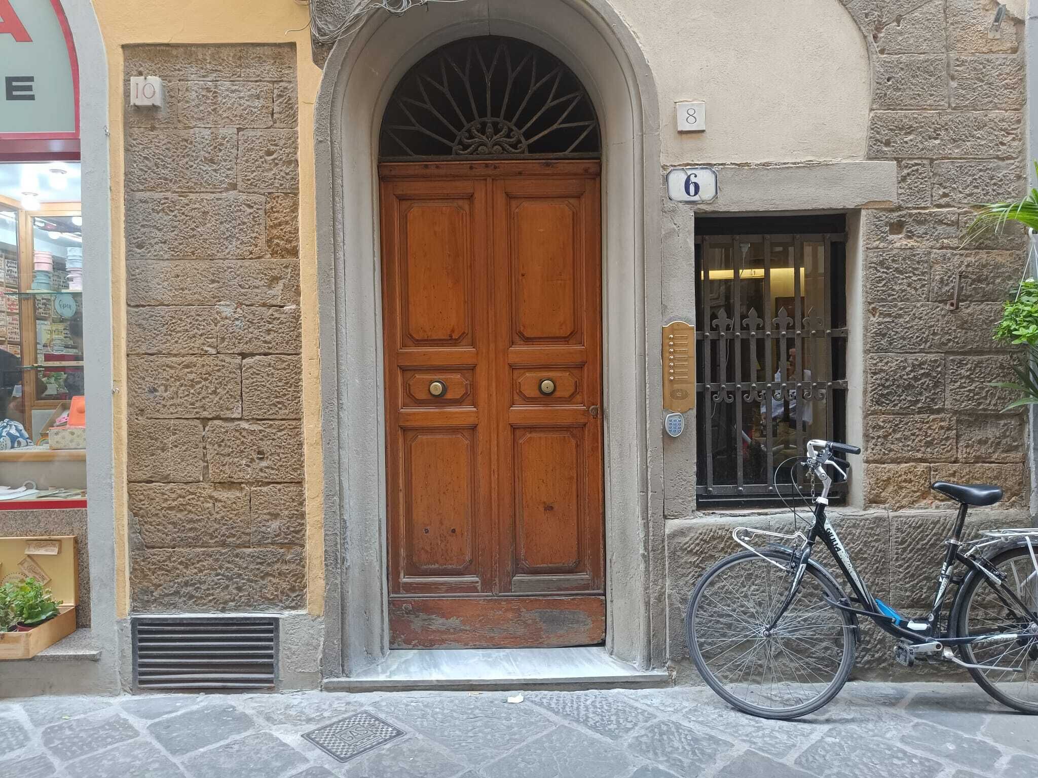Un edificio de piedra con una puerta doble de madera, una bicicleta estacionada afuera y una ventana pequeña con un letrero con el número '6'.