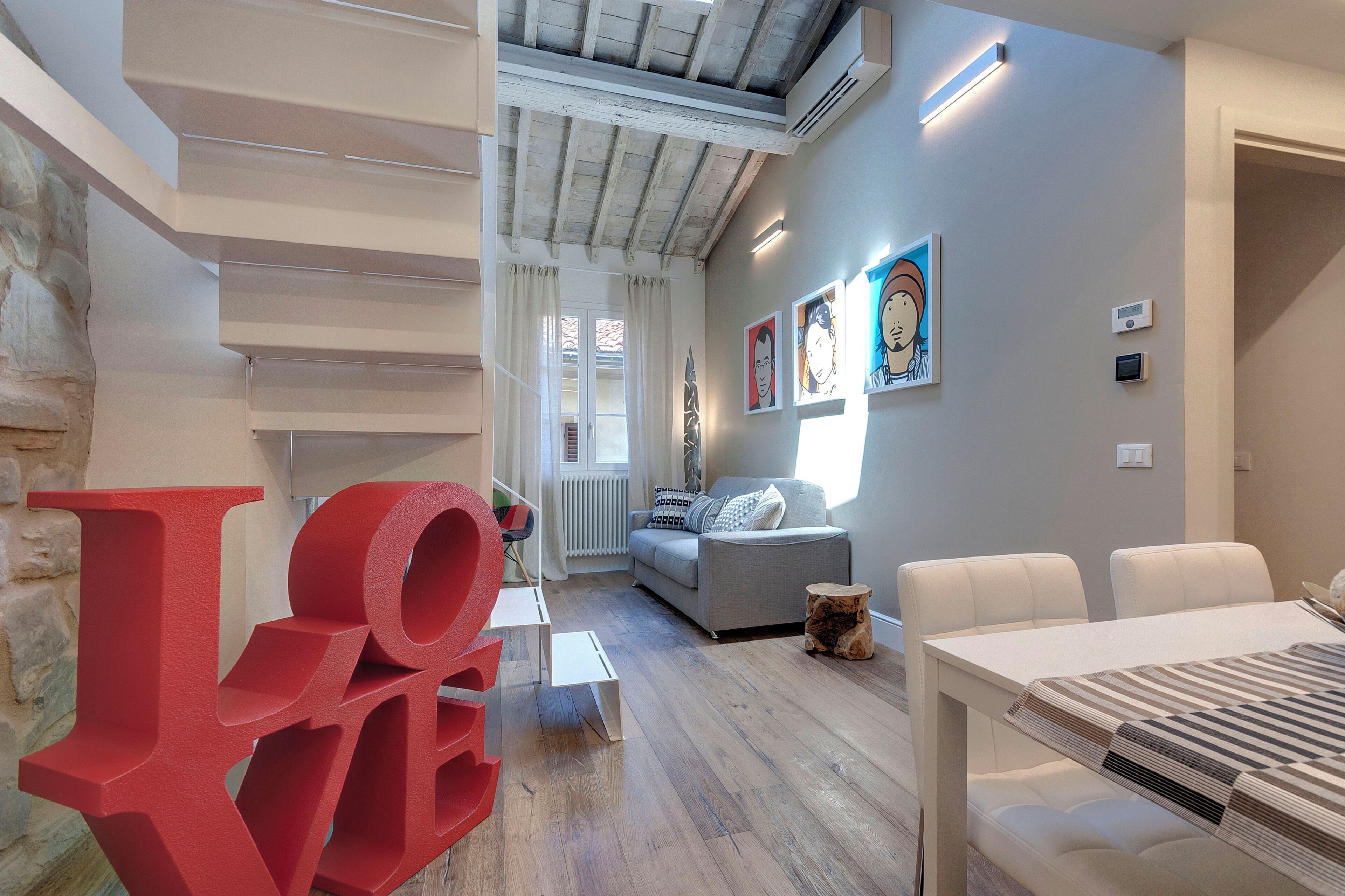 Una sala de estar moderna con una escalera, un sofá, una mesa de comedor y obras de arte en las paredes.