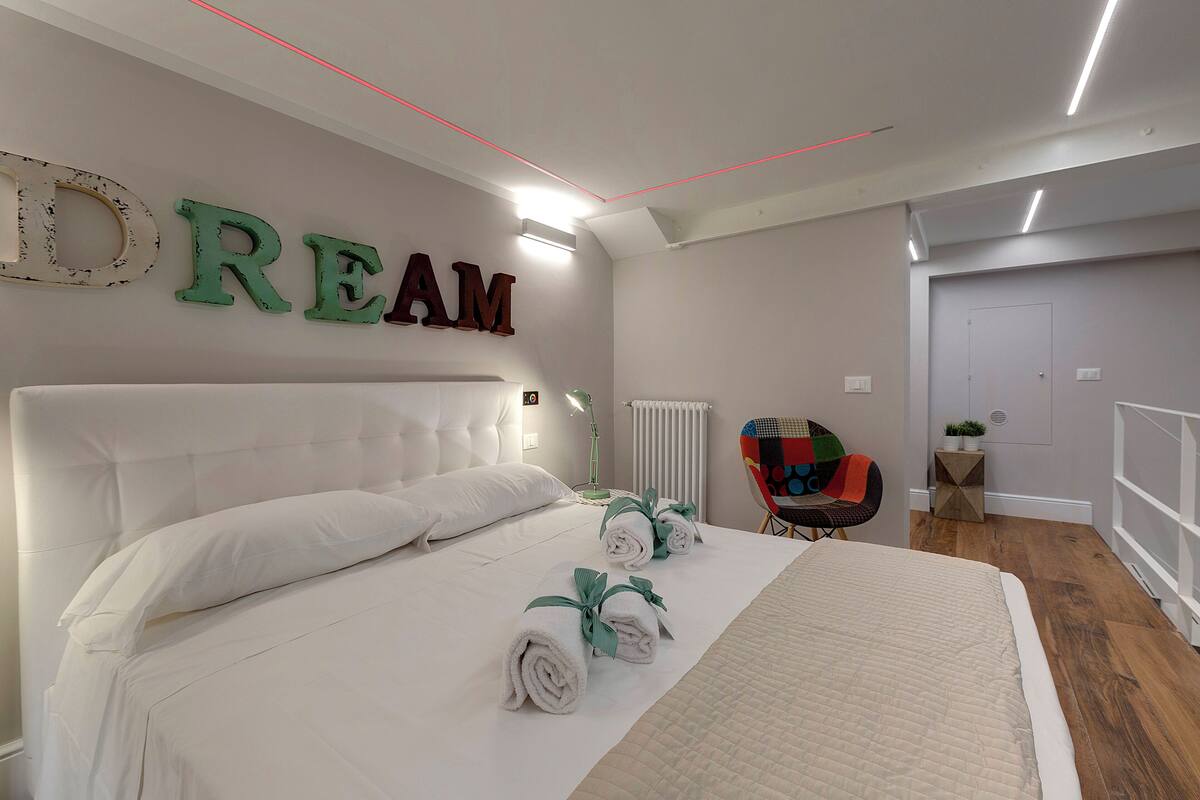 Ein Schlafzimmer mit einem großen Bett, einem an der Wand befestigten Schild mit der Aufschrift 'DREAM', einem Sessel und einem kleinen Tisch mit einer Pflanze.