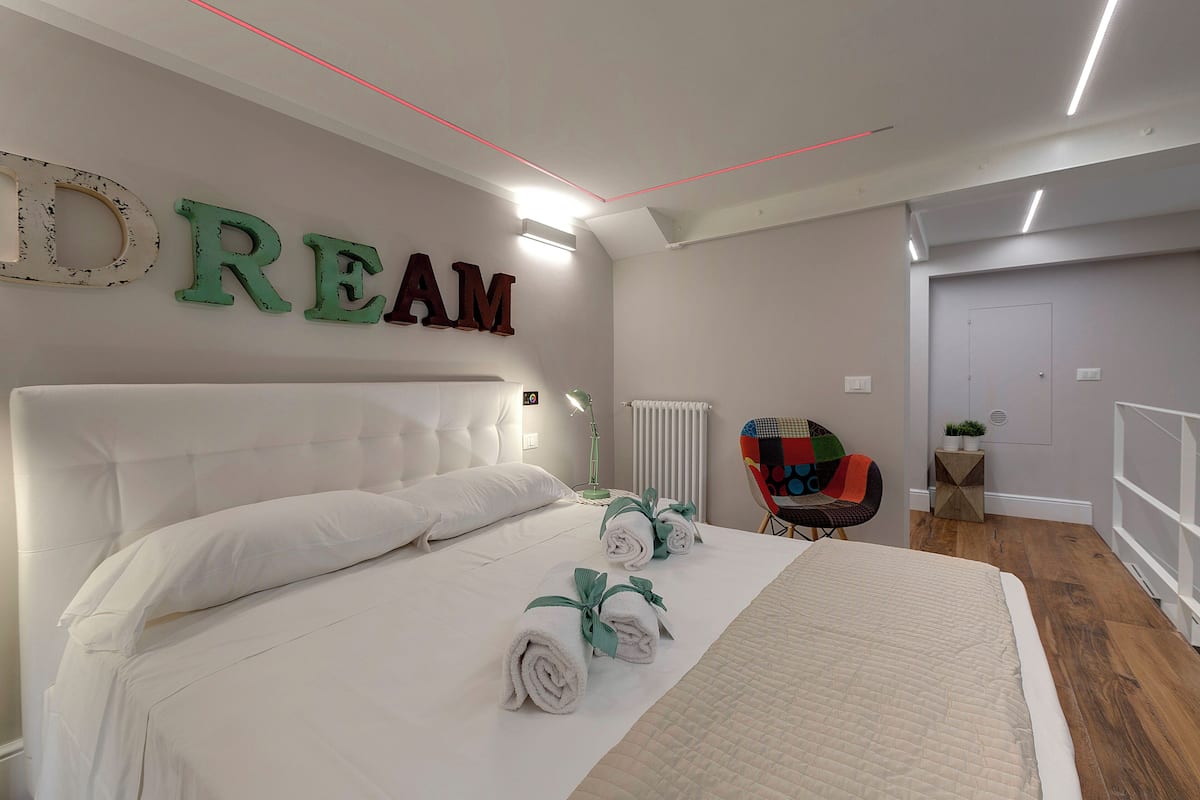 Ein Schlafzimmer mit einem großen Bett, einem an der Wand befestigten Schild mit der Aufschrift 'DREAM', einem Sessel und einem kleinen Tisch mit einer Pflanze.