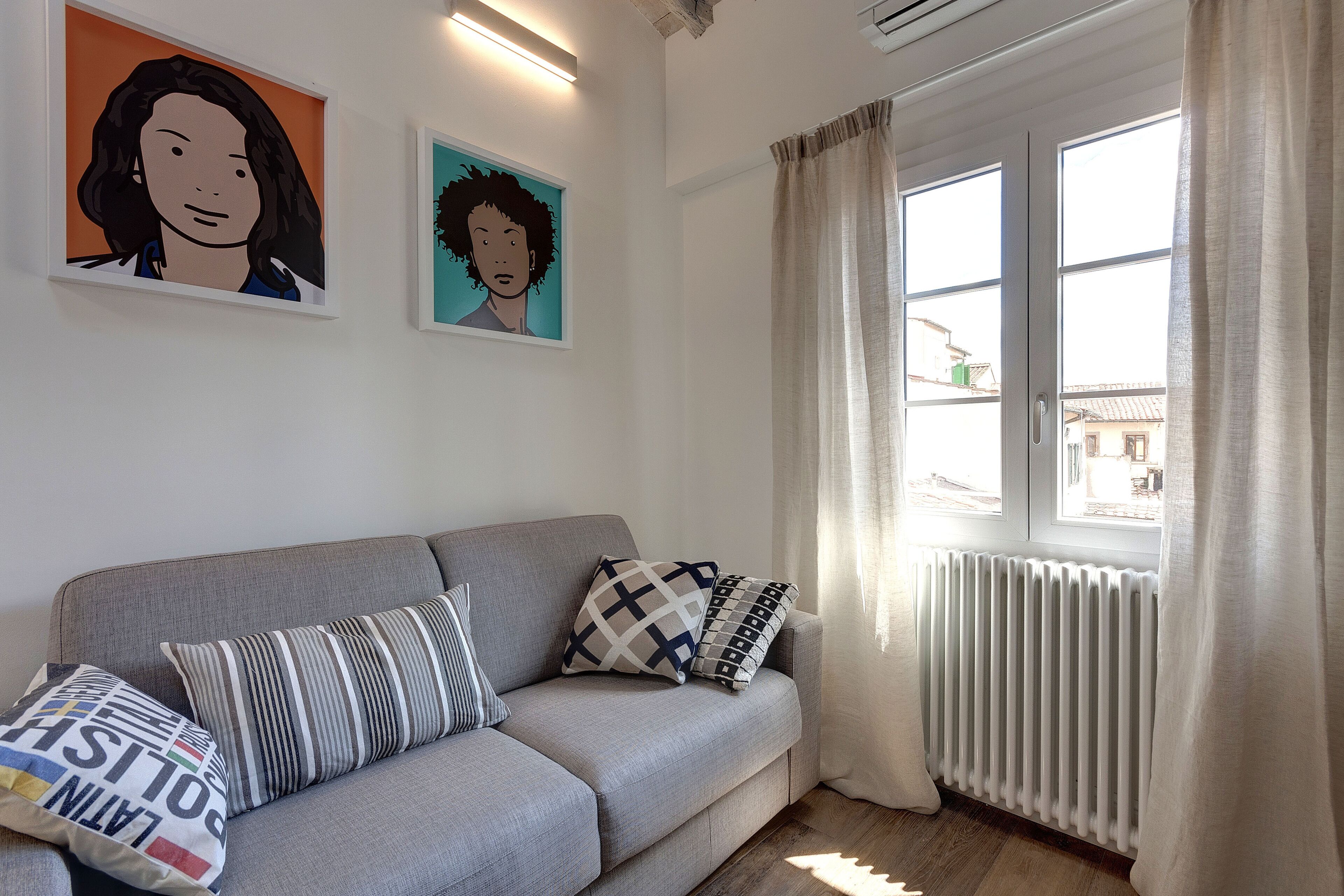 A living room with a grey sofa, striped and patterned cushions, and two framed artworks on the wall.