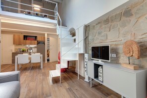 A modern interior with a dining area, staircase, stone wall, and a flat-screen TV.