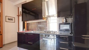 A modern kitchen with stainless steel appliances, black cabinets, and a tiled backsplash. - Mamo Florence - Binario 9 Apartment (Florence)