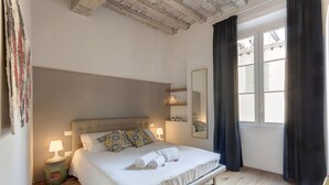 Ein Schlafzimmer mit einem Bett, Nachttischlampen, einem Nachttisch, einem Fenster mit Vorhängen und einem Spiegel an der Wand.