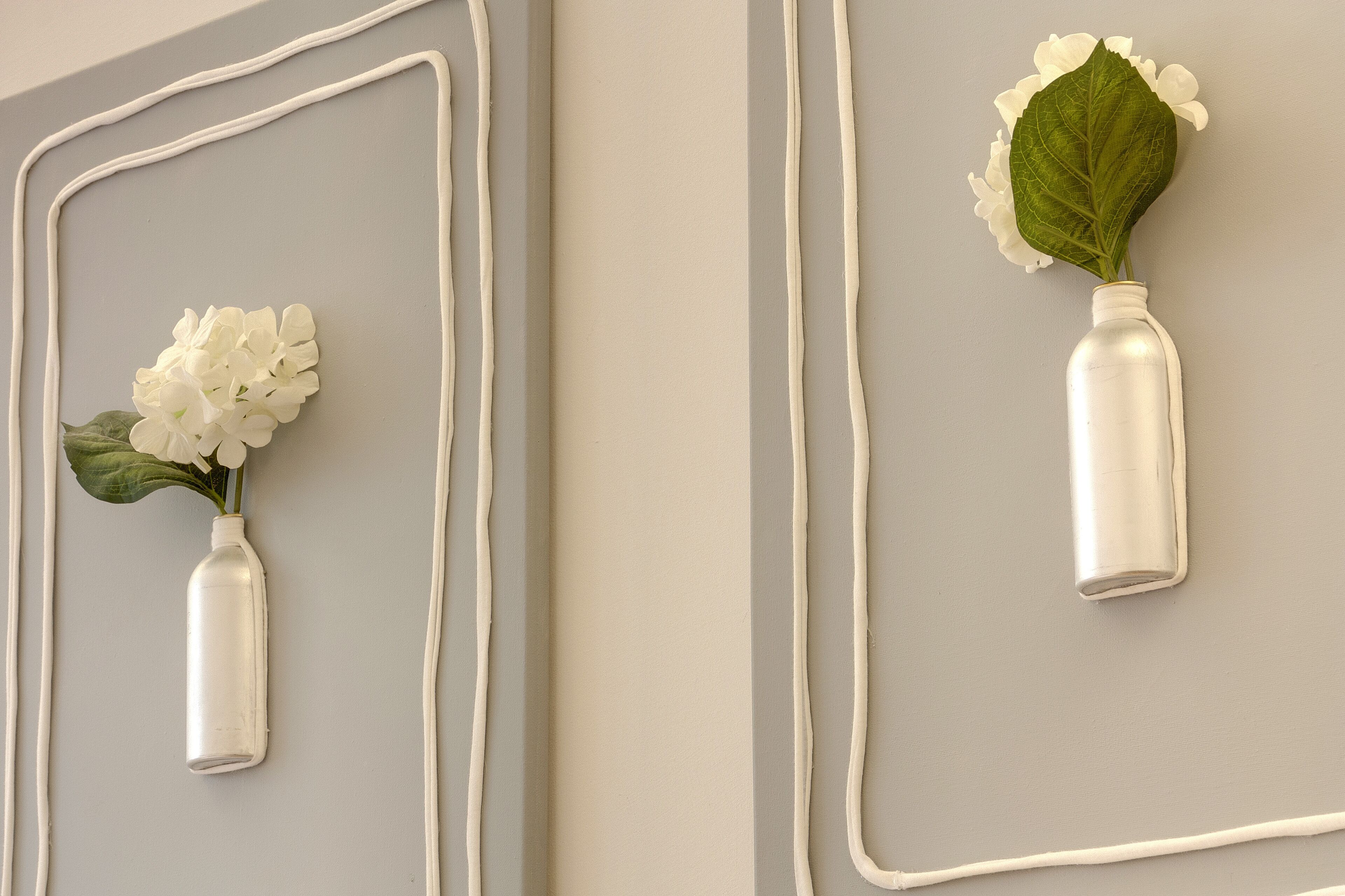 Two white vases with flowers and leaves mounted on a wall with a geometric design.