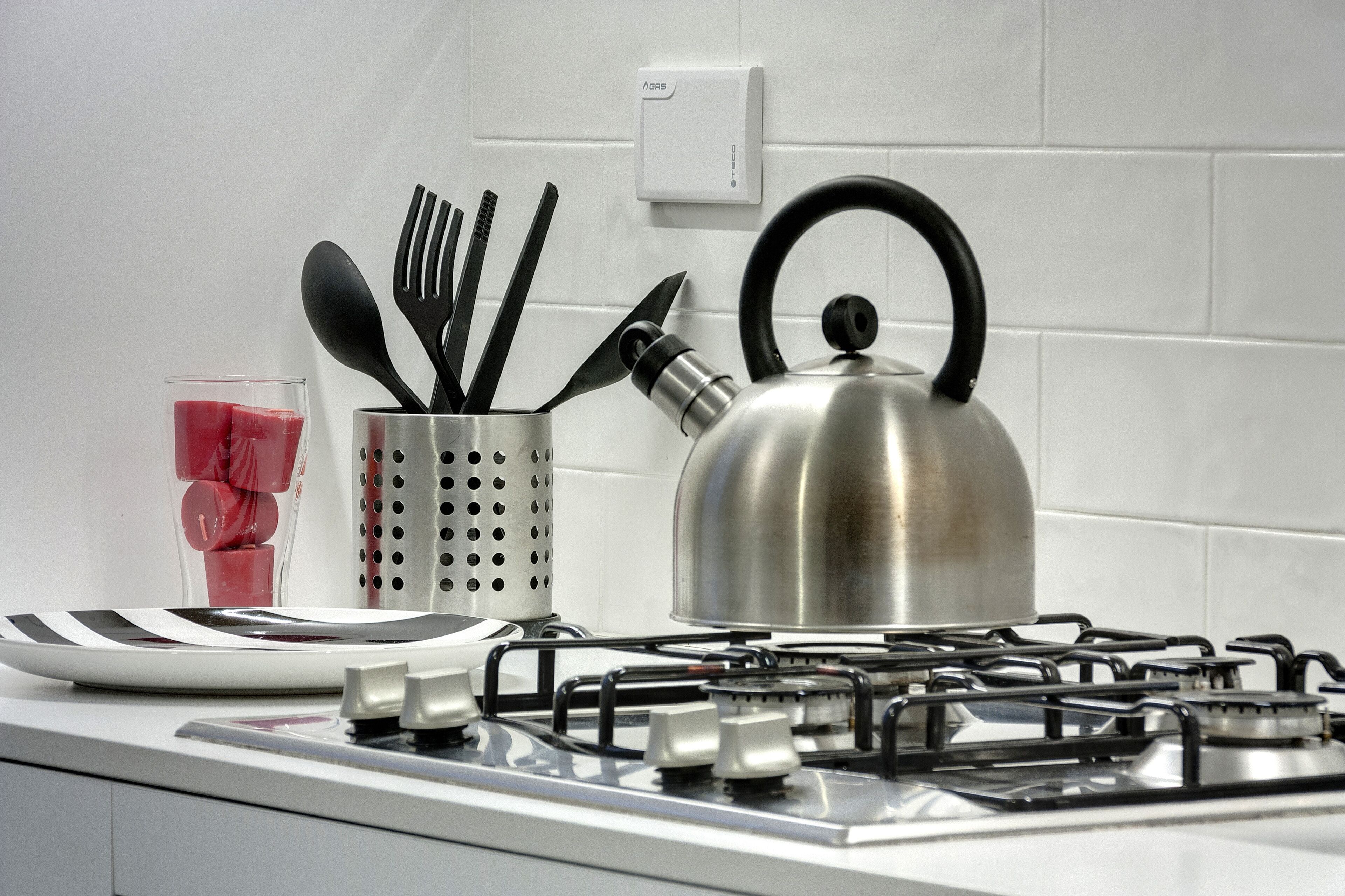 Une cuisine équipée d’une cuisinière à gaz, d’une bouilloire, d’un verre contenant une boisson rouge et d’un porte-ustensiles.