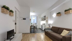A modern living room with a brown sofa, a flat-screen TV, wooden flooring, and built-in wooden shelves with plants. - Mamo Florence - Costa San Giorgio Apartment (Florence)