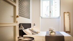 A hotel room with a bed, bedside table, lamp, and a window with a view of buildings. - Mamo Florence - Costa San Giorgio Apartment (Florence)