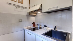 A kitchen with white cabinets, a black sink, and a stainless steel range hood. - Mamo Florence - Cupolone Apartment (Florence)