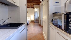A narrow hallway with a kitchen area on one side, a bed on the other, and a visible thermostat on the wall. - Mamo Florence - Cupolone Apartment (Florence)