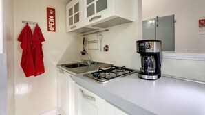 Una cocina con armarios blancos, estufa a gas, cafetera y toallas rojas colgadas en ganchos.