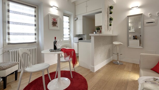 Un salón moderno y luminoso con una mesa de comedor, sillas, alfombra roja y sofá blanco.