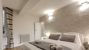 Una cama bien hecha con almohadas y toallas, un radiador blanco y una ventana con cortinas.