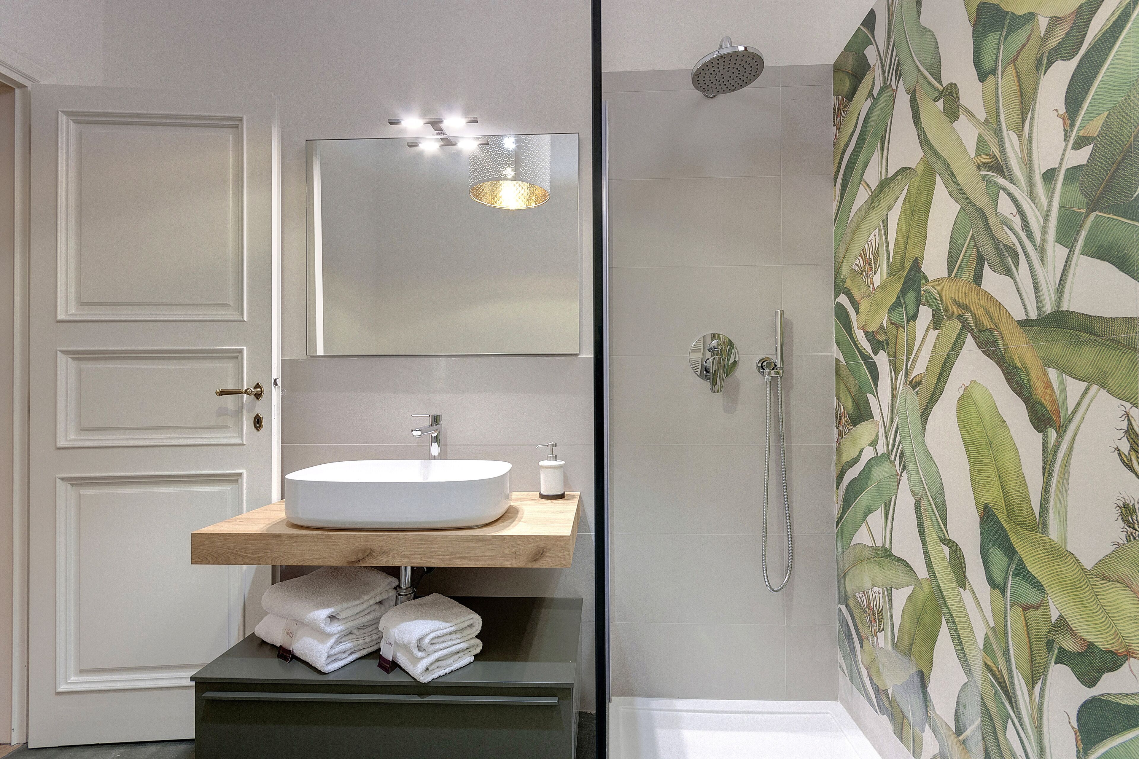 Een badkamer met een witte wastafel, een spiegel en een douche met een muur gedecoreerd met planten.