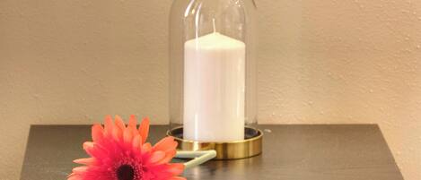 A candle in a glass dome on a wooden table with a single flower beside it.
