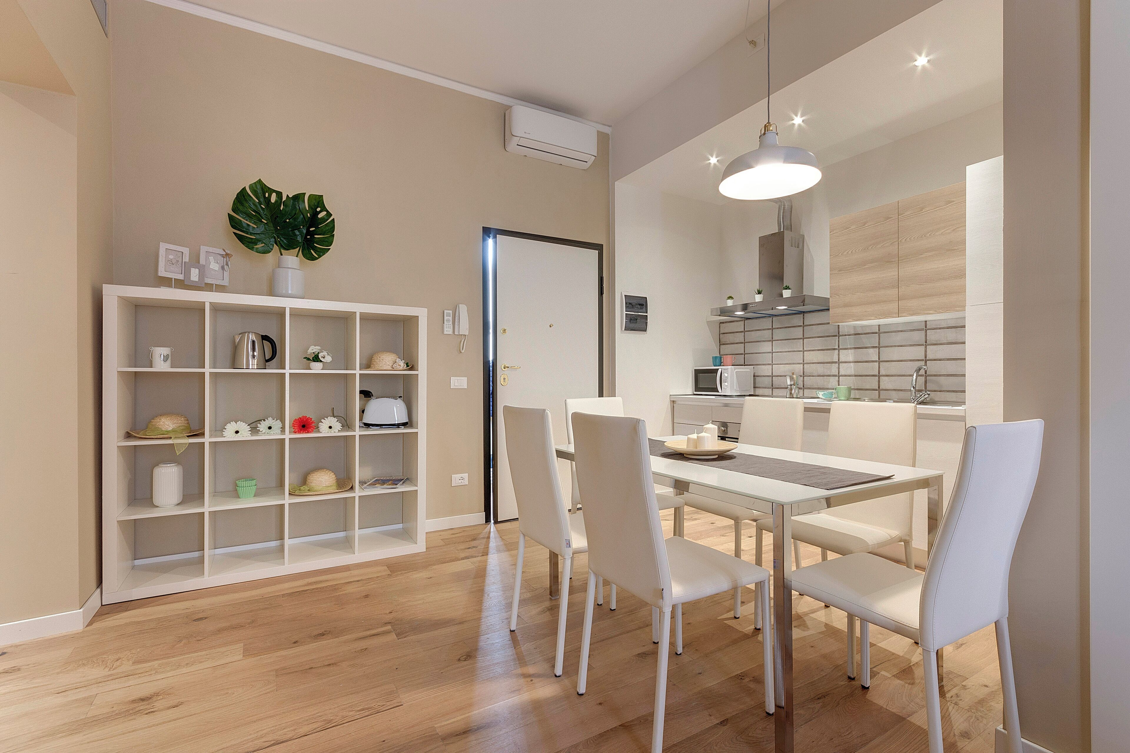 A modern kitchen with white cabinetry, a dining area with a white table and chairs, and a built-in shelving unit with various kitchen items.