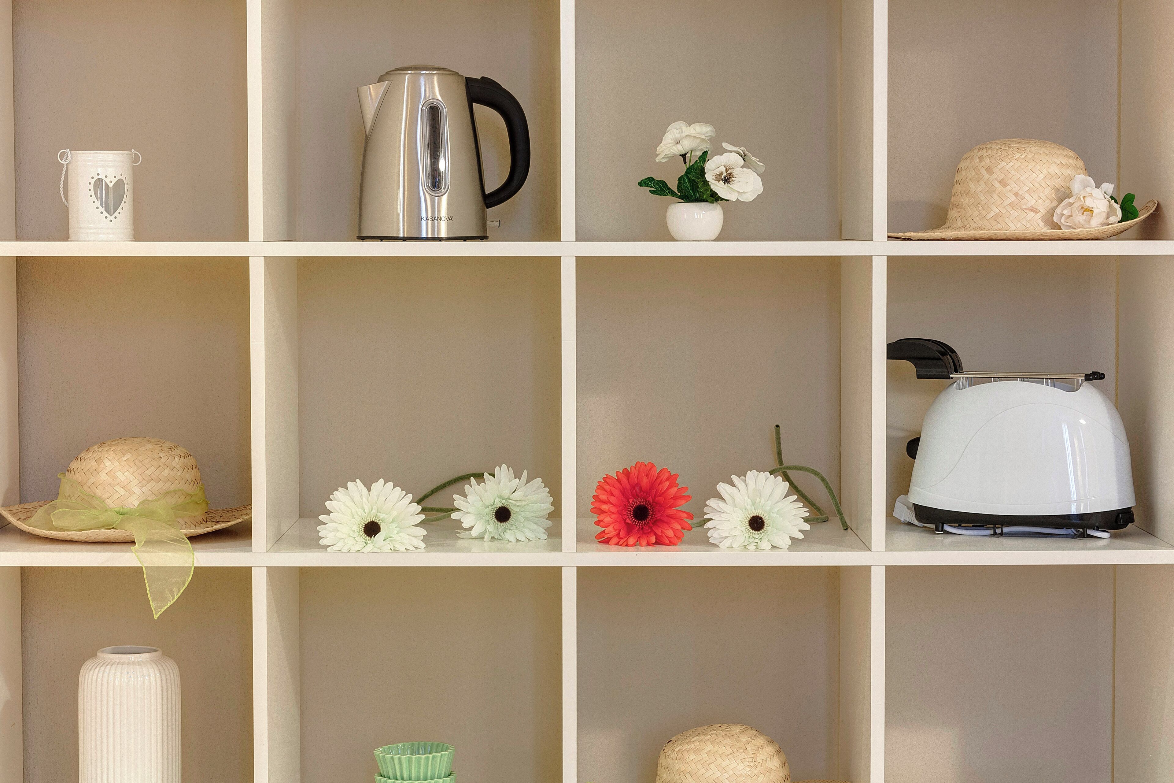 A neatly organized shelf with various items including a kettle, a hat, flowers, and a vase.