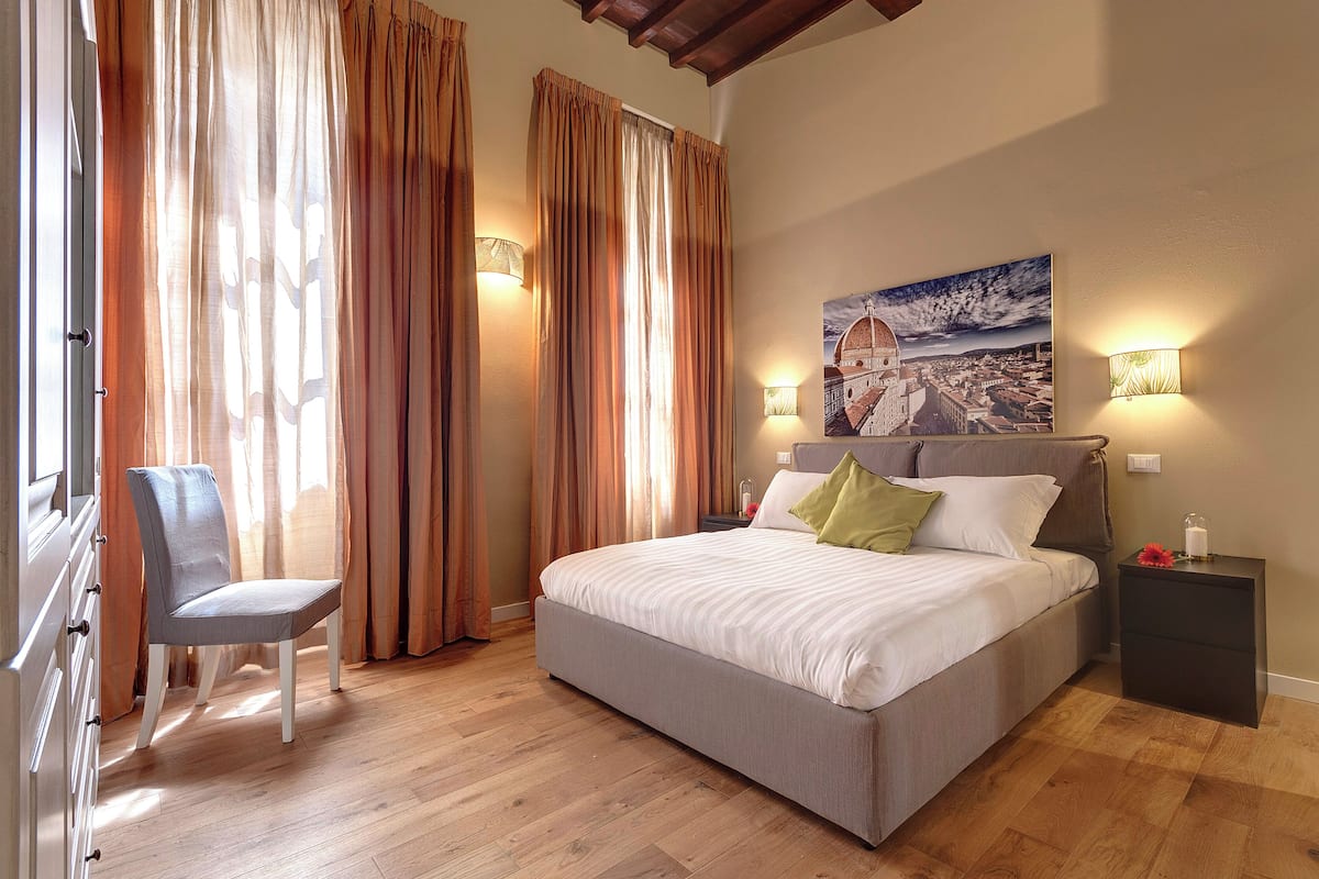 A bedroom with a bed, a chair, a nightstand, and a painting on the wall.