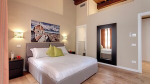 Een slaapkamer met een groot bed, twee nachtkastjes, een wandlamp, een schilderij en een deur met een spiegel.