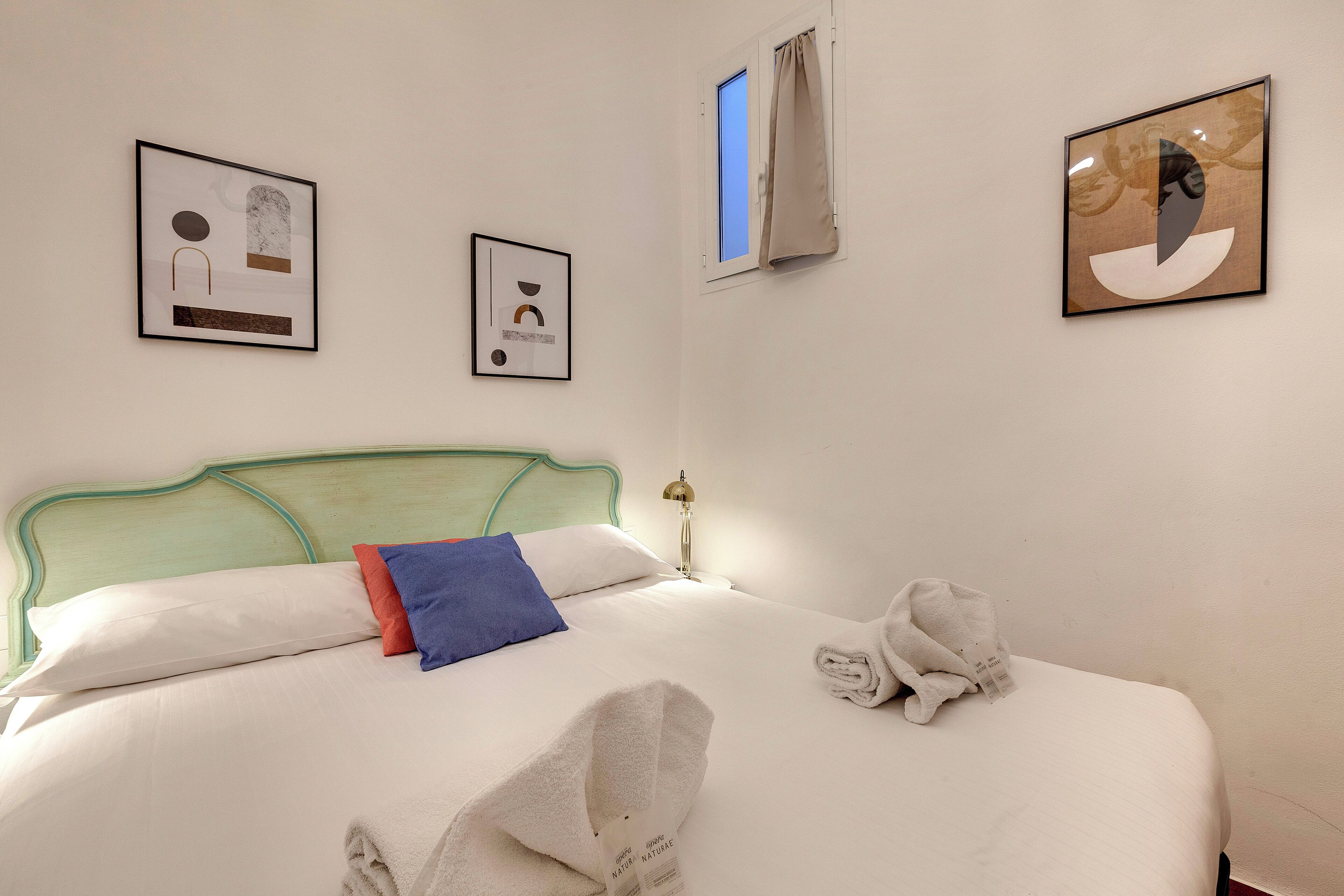 A neatly made bed with a green headboard, white and blue pillows, and a pair of towels on the side.