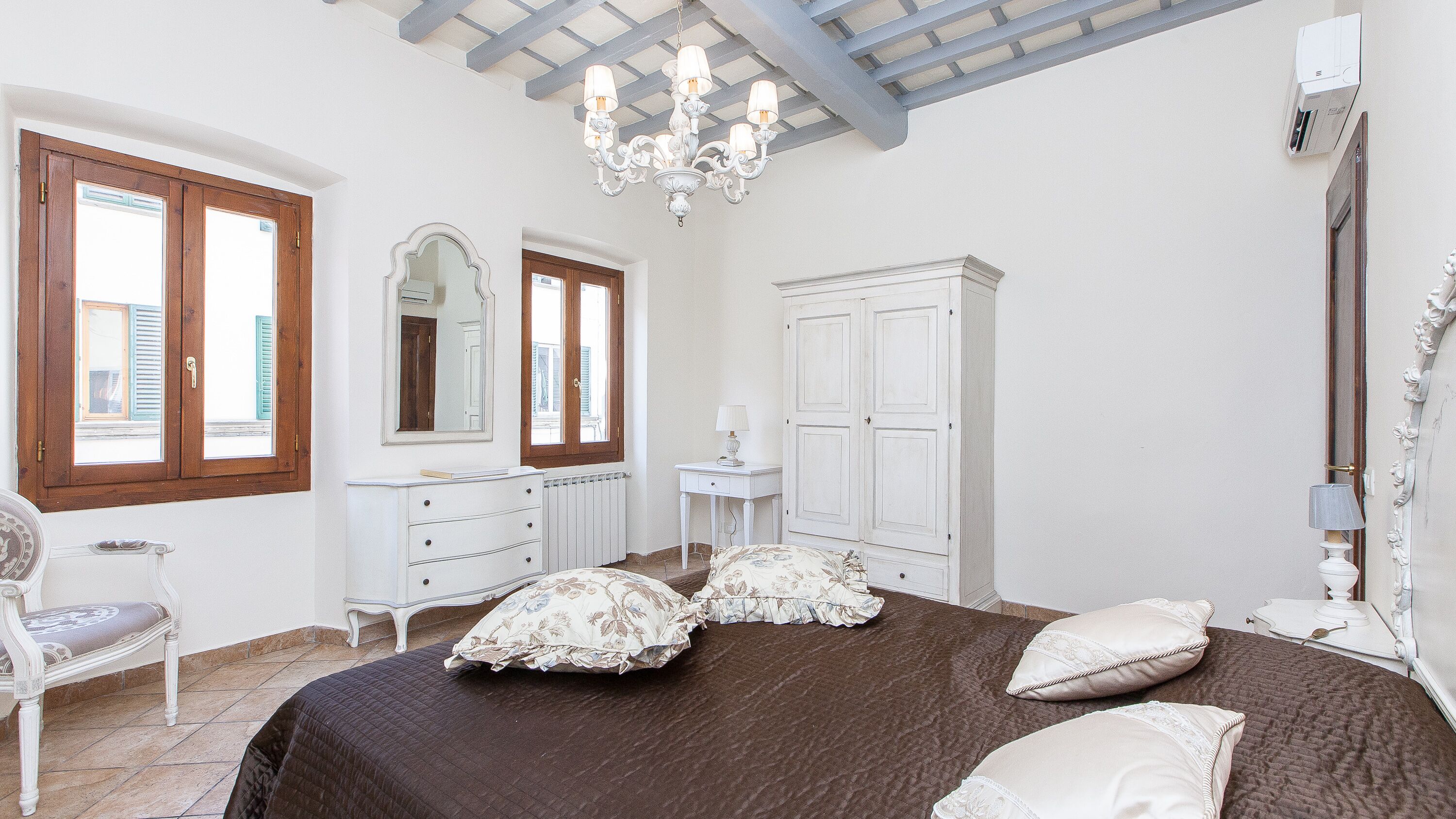 A bedroom with a large bed, a dresser, a mirror, and a chandelier.