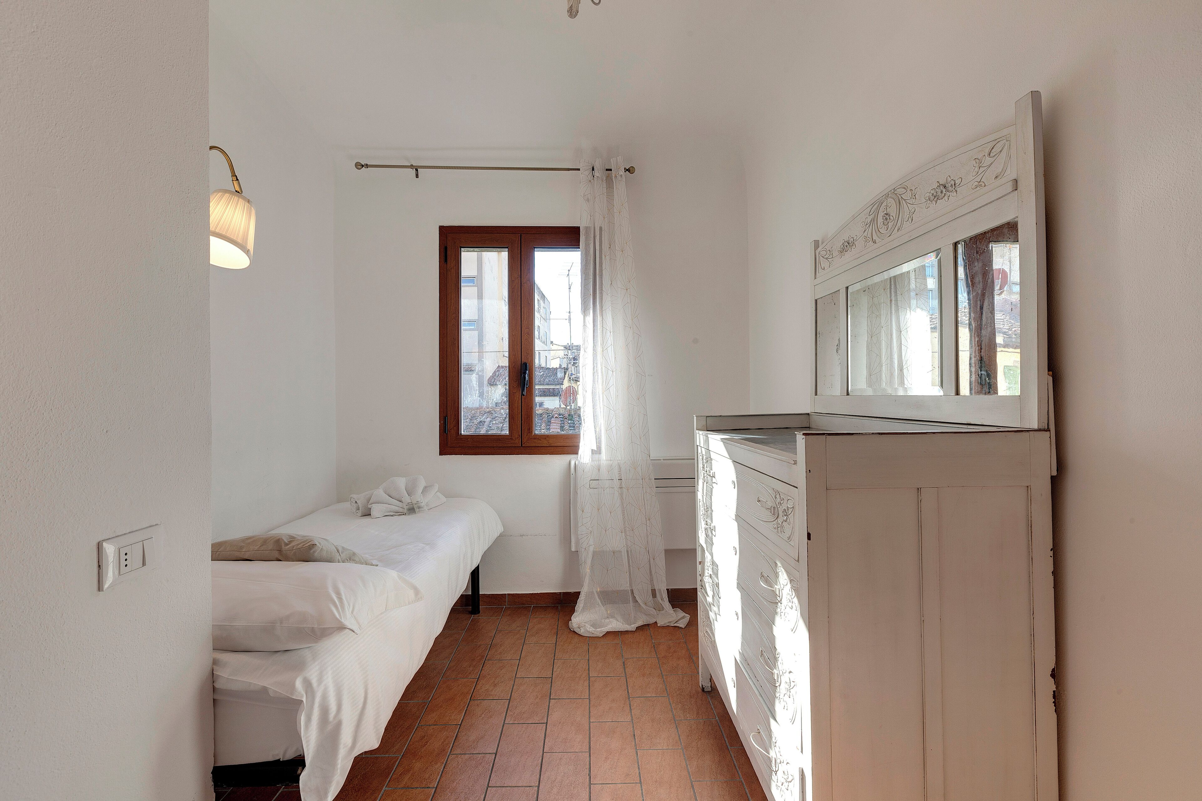 A small, clean room with a bed, a dresser, and a window with curtains.