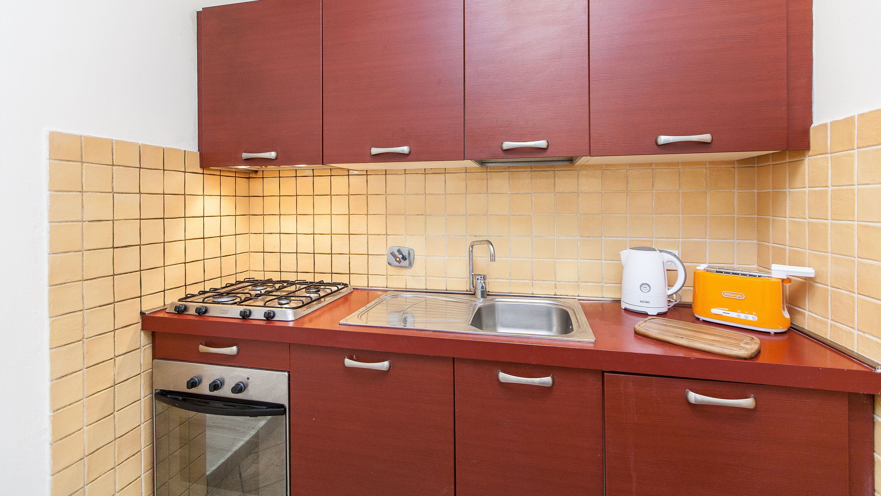 A compact kitchen with a gas stove, a sink, a kettle, and a toaster.