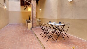 A patio with a table and chairs, a hanging plant, and a brick wall. - Mamo Florence - Palazzuolo Tower (Florence)