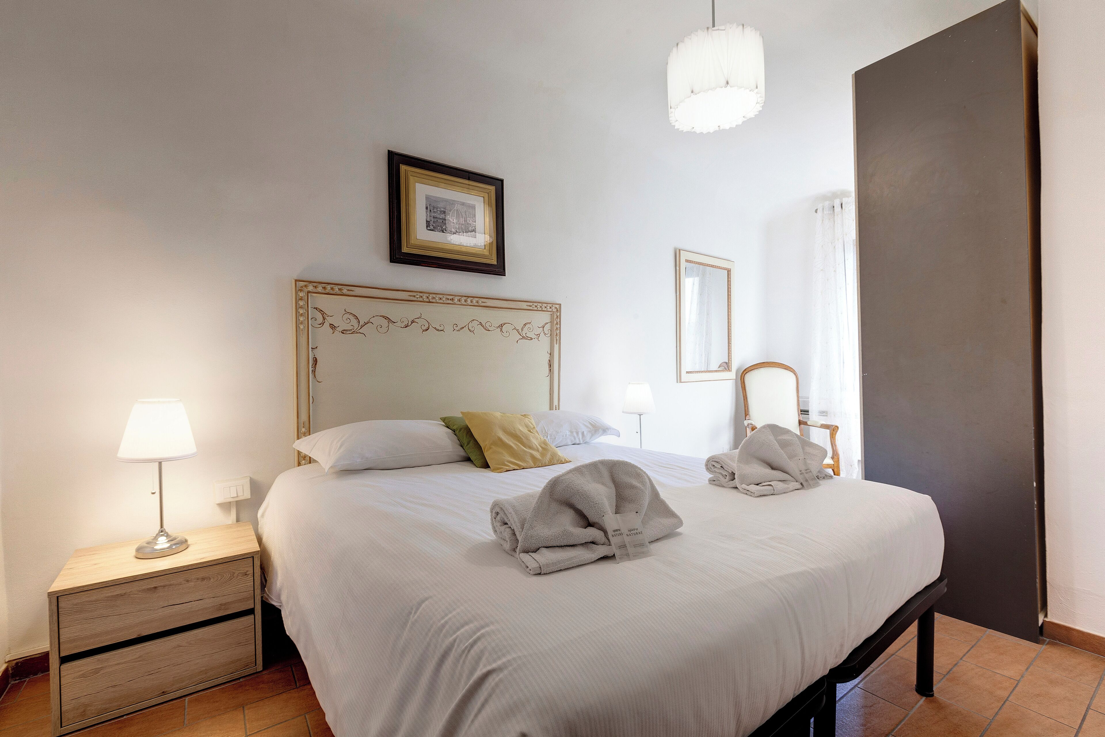 A neatly made bed with a headboard, a bedside table with a lamp, and a framed picture on the wall.