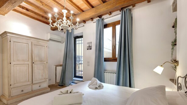 A bedroom with a large bed, a wooden ceiling, a chandelier, and a wardrobe. - Mamo Florence - Palazzuolo Tower (Florence)