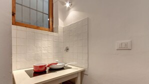 Une cuisine avec des carreaux blancs, une fenêtre et un plan de travail sur lequel se trouvent une casserole rouge et une poêle blanche.