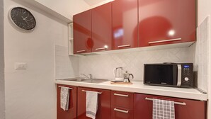 Une cuisine avec des placards rouges, un four à micro-ondes et une horloge au mur.