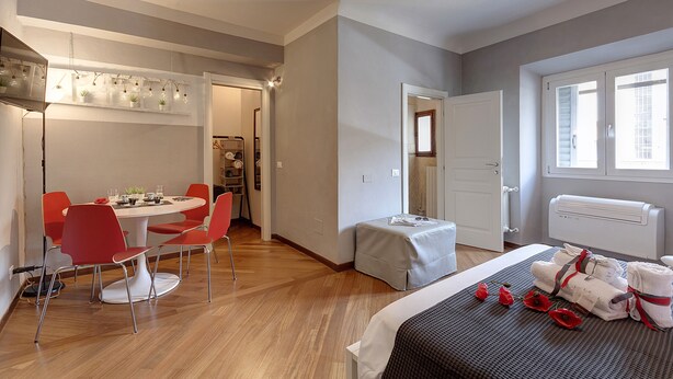 Une chambre d’hôtel avec un lit, une petite table avec des chaises, une table de chevet avec des serviettes et une fenêtre avec des stores.