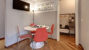 Un coin repas avec une table ronde, des chaises rouges, un téléviseur à écran plat et une étagère ornée de plantes et de lampes.
