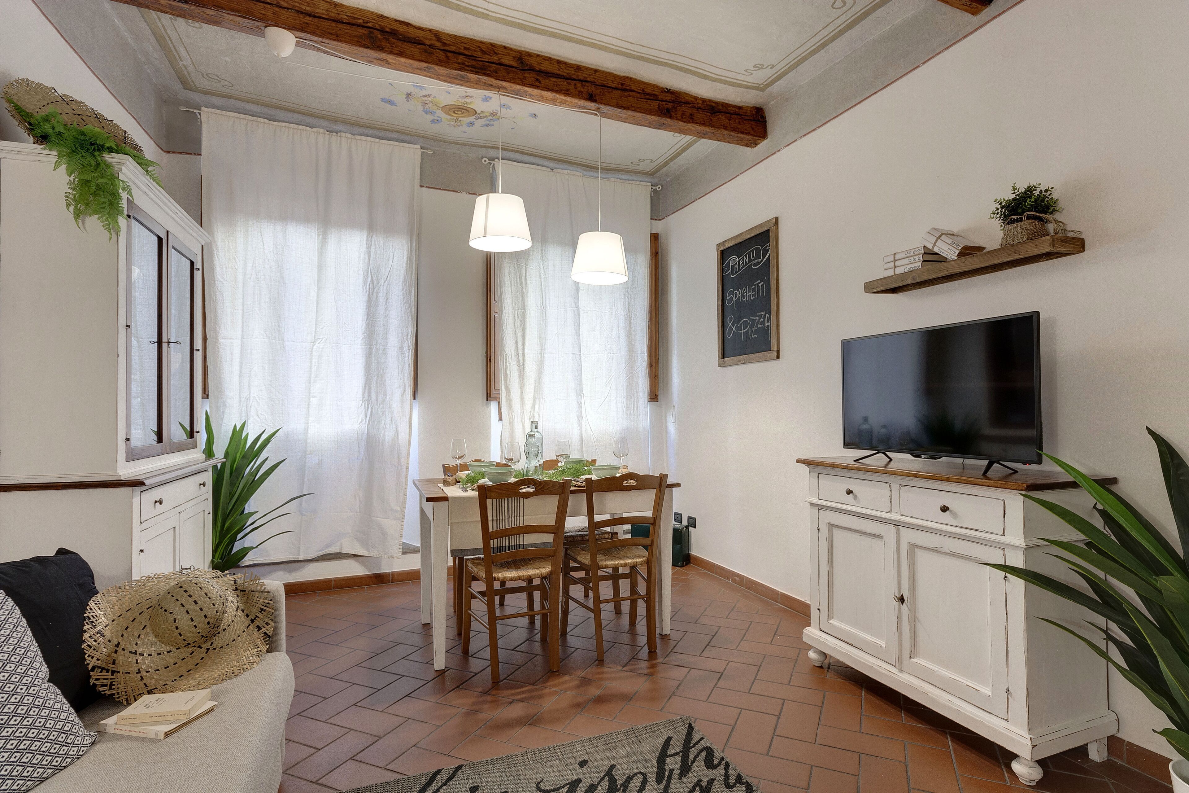A dining area with a wooden table and chairs, a television on a cabinet, and a large plant.