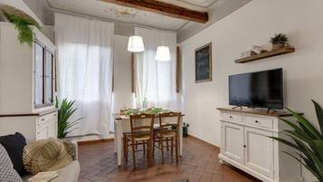A dining area with a wooden table and chairs, a television on a cabinet, and a large plant.