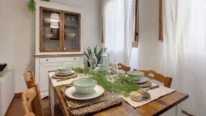 A dining area with a wooden table set for four, surrounded by chairs. A cabinet with glass doors is visible in the background. - Mamo Florence - Ghibellina Apartment (Florence)